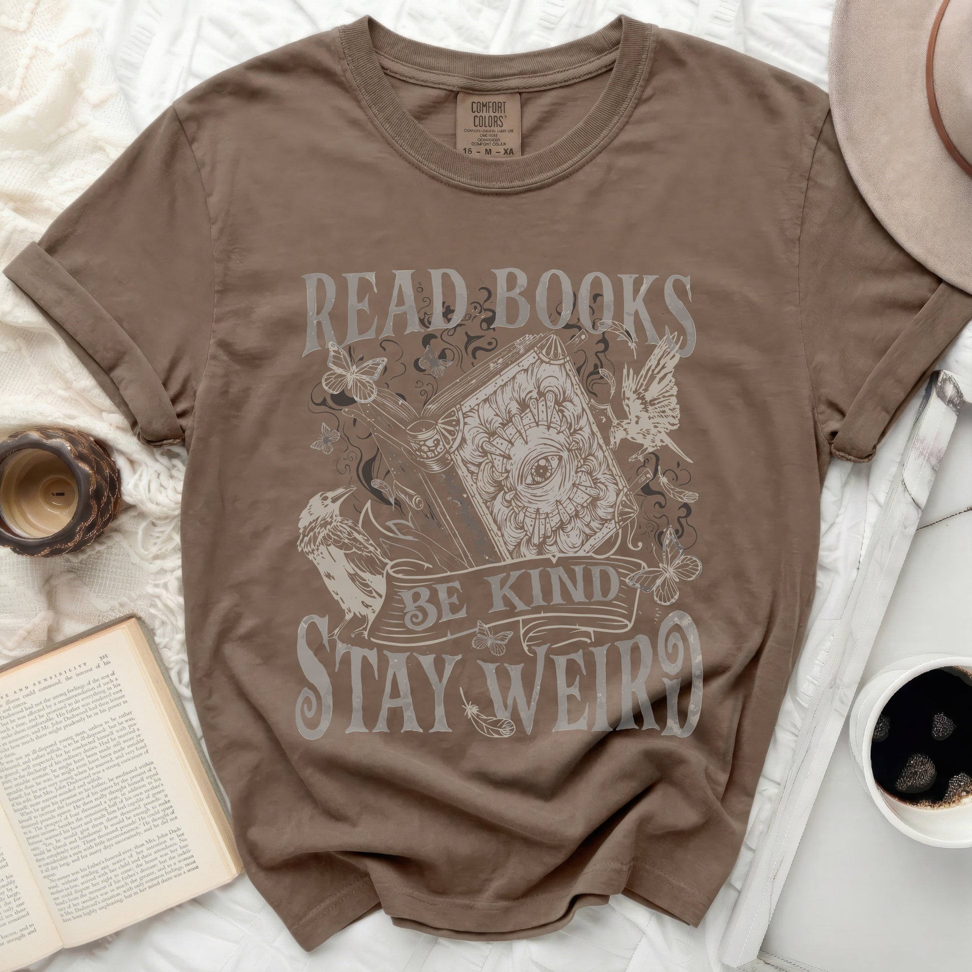 Brown t-shirt with "Read Books Be Kind Stay Weird" text and vintage illustrations.