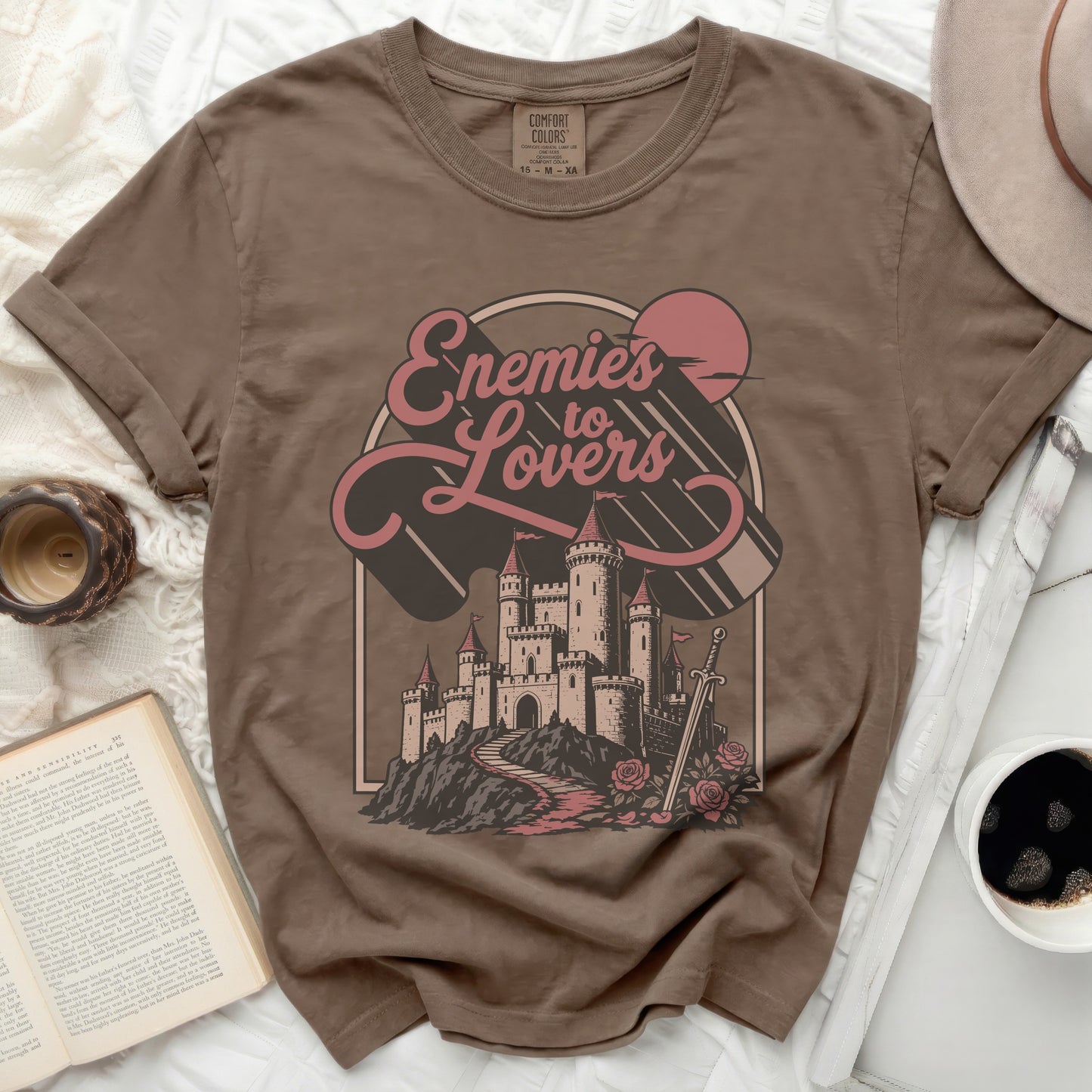 Brown t-shirt graphic of castle, sword, roses, and "Enemies to Lovers".