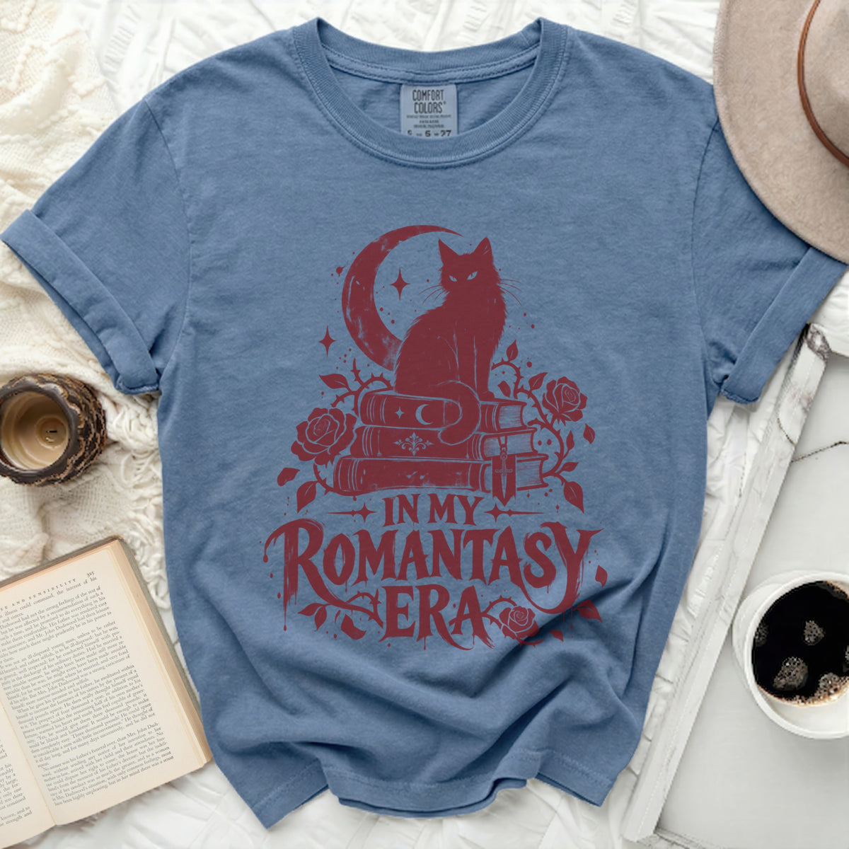 Blue t-shirt with red graphic of cat on books, moon, roses, and text "IN MY ROMANTASY ERA".