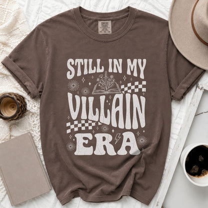 Brown t-shirt with white text "STILL IN MY VILLAIN ERA" and floral graphics.