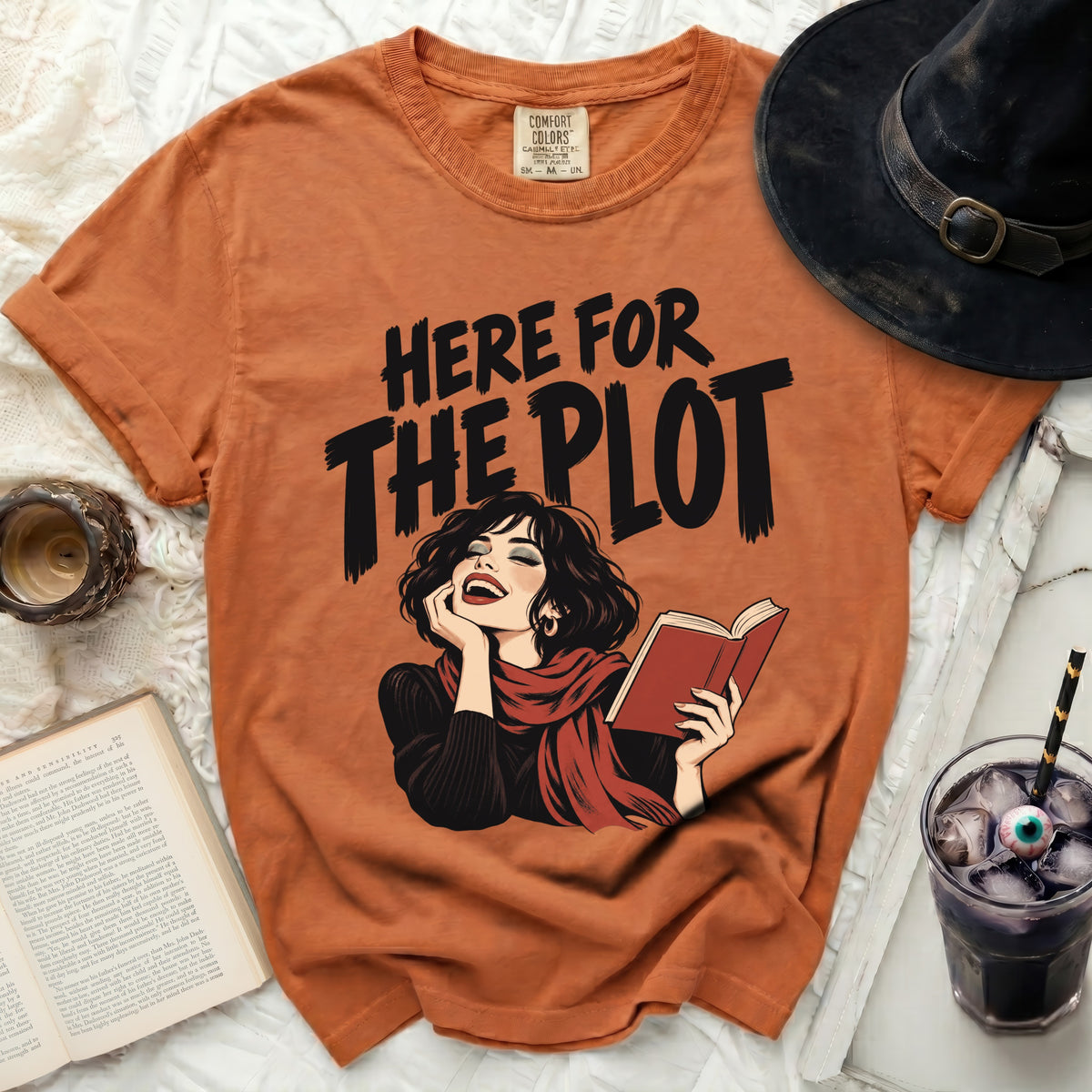 Orange t-shirt with "HERE FOR THE PLOT" graphic featuring a laughing woman reading a book.