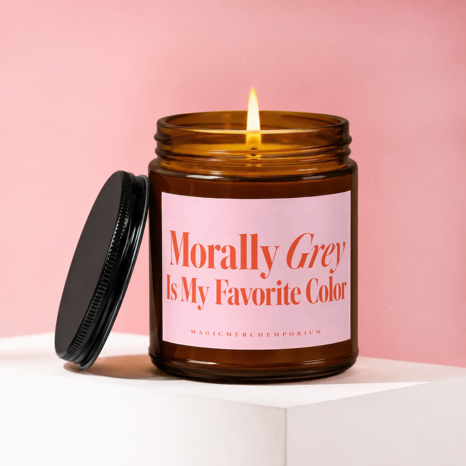 Amber candle with lit flame, black lid, and pink label reading "Morally Grey Is My Favorite Color".