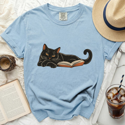 Light blue t-shirt with a black cat illustration lying on an open book.