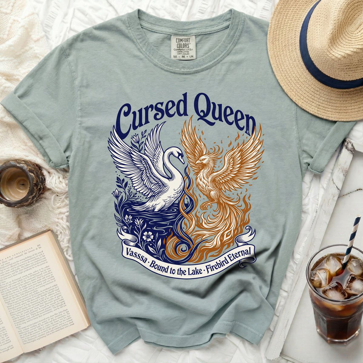 Light blue t-shirt with "Cursed Queen" text, swan, and phoenix graphic, and banner text.