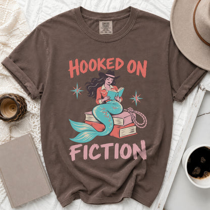 Brown t-shirt with "Hooked on Fiction" text and a mermaid reading a book.