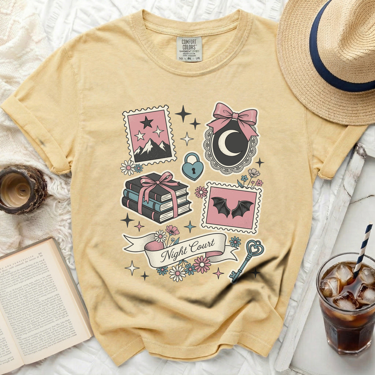 Yellow t-shirt with "Night Court" and graphic designs of stamps, books, and celestial elements.