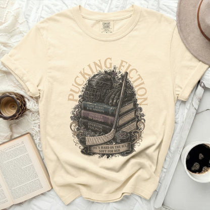 Cream t-shirt with "Puckin' Fiction" text and hockey gear over books.