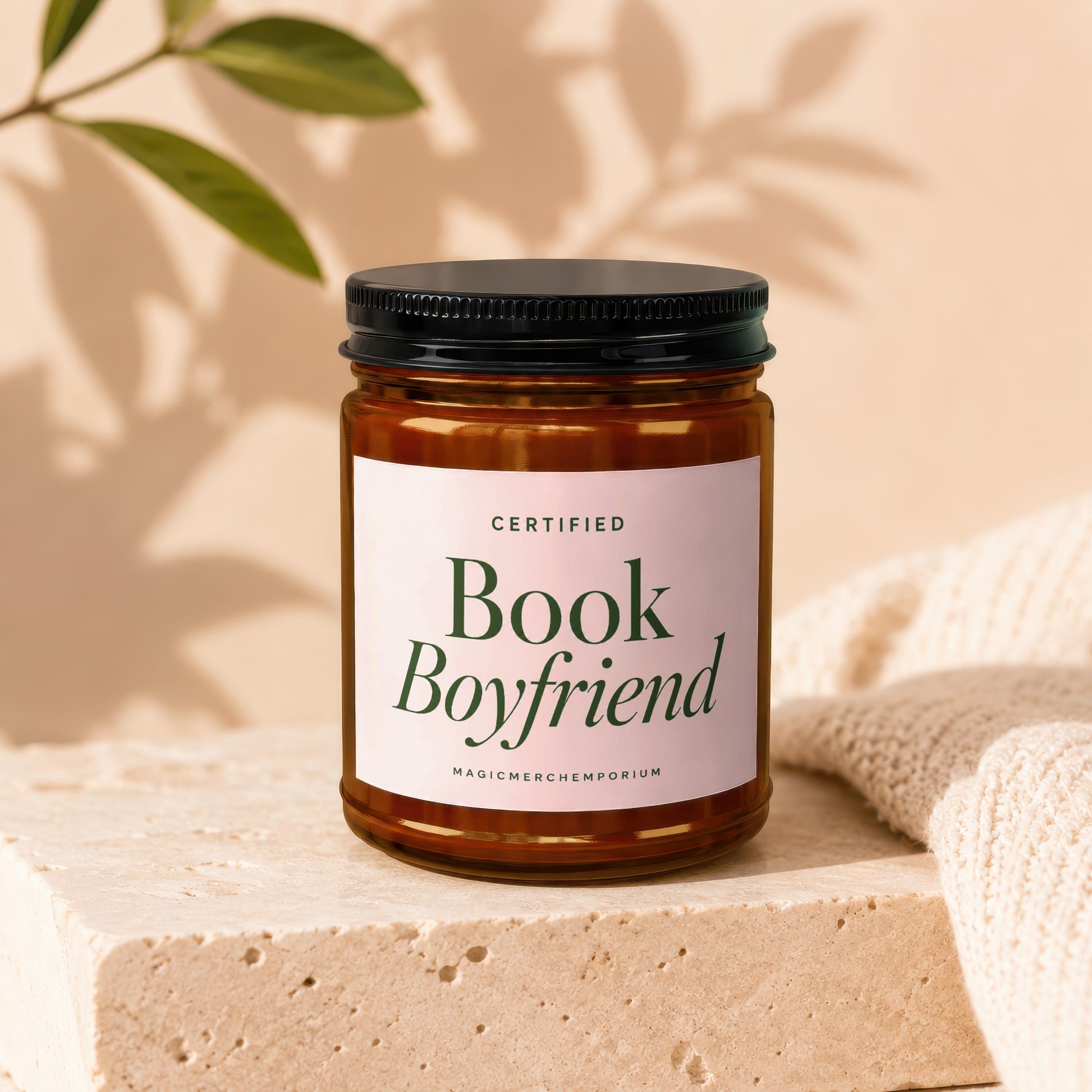 Amber jar candle with "Certified Book Boyfriend" label on stone block with knit fabric.
