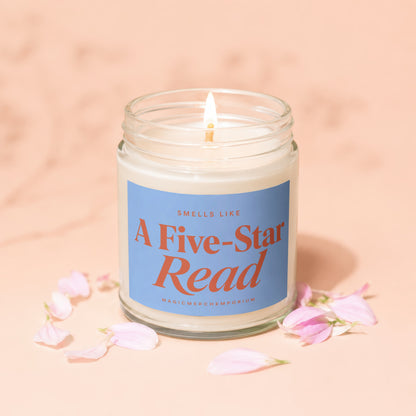 Lit candle in glass jar with blue label reading "Smells Like A Five-Star Read".