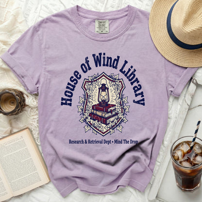 Purple t-shirt with "House of Wind Library" crest, lantern, and books graphic.