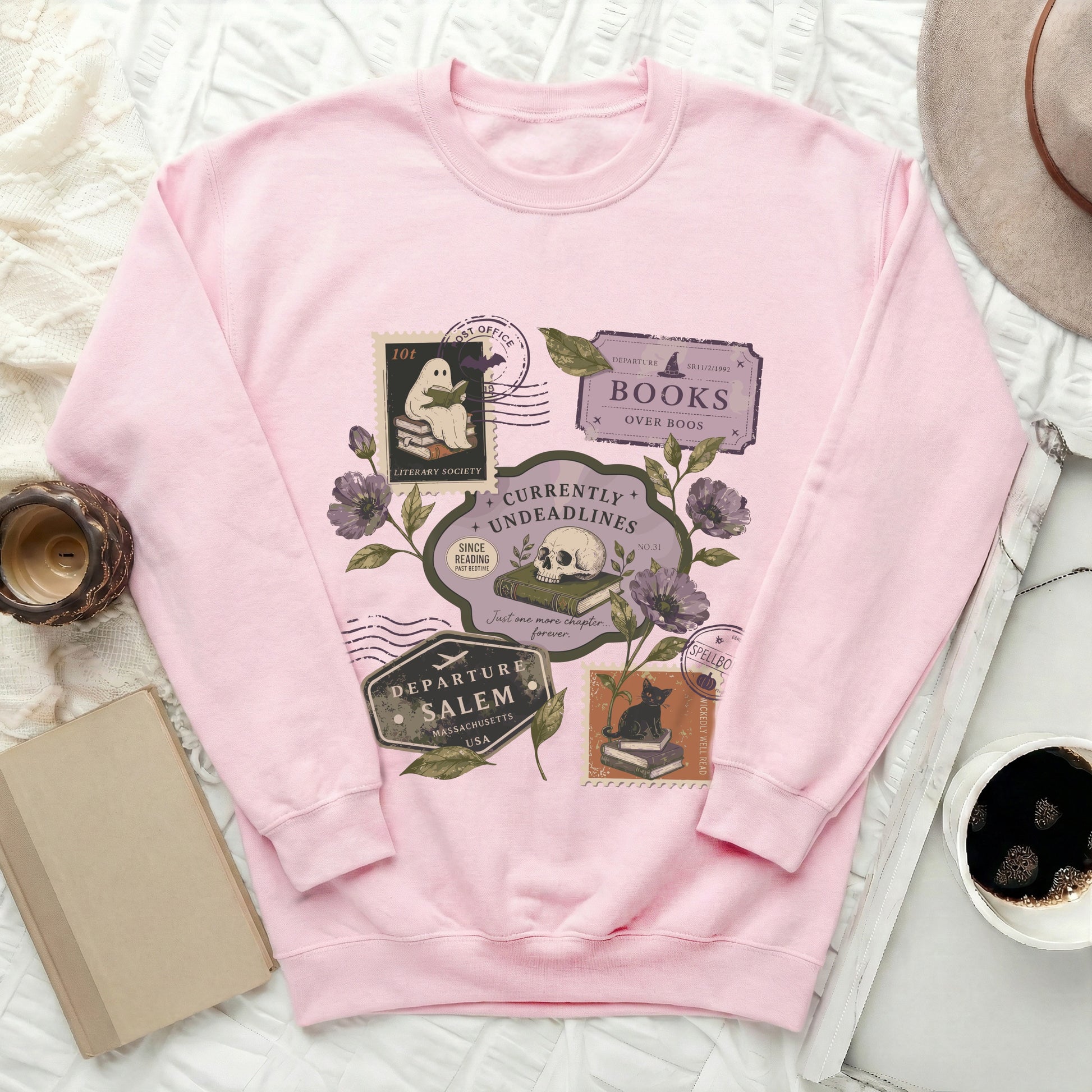 Pink sweatshirt with vintage spooky book-themed stamps featuring a ghost, skull, and cat.