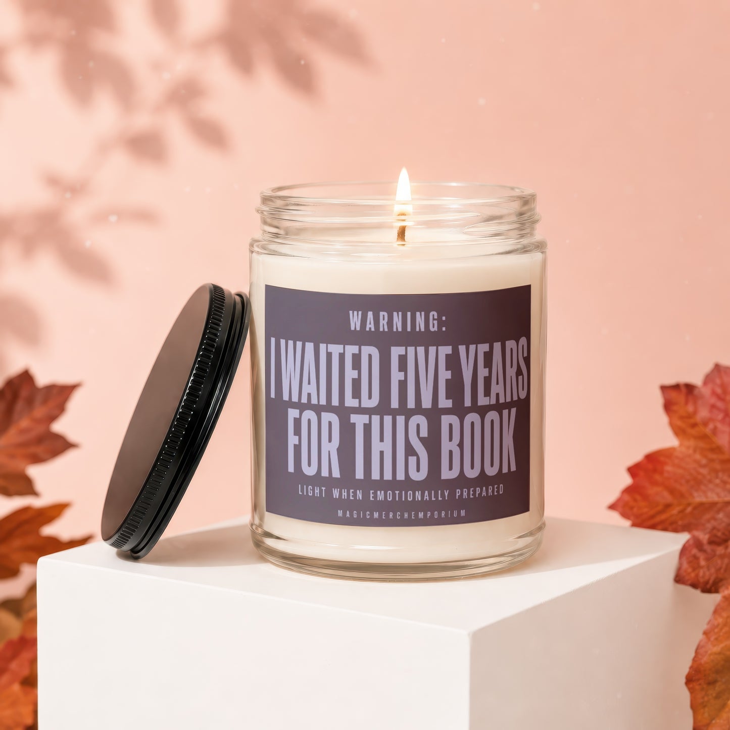Candle with lid off, "I waited five years for this book" text, lit wick.