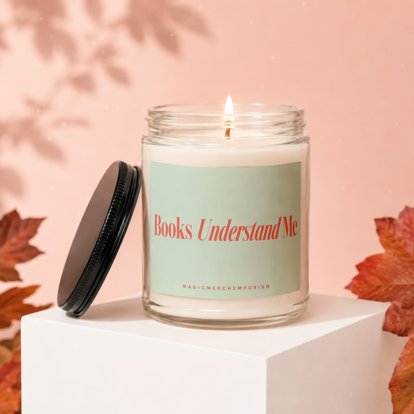 Glass candle with lit wick, light green label reading "Books Understand Me".