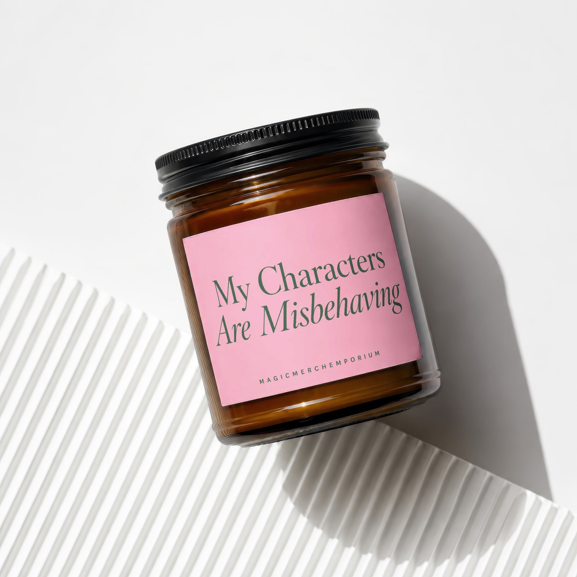 Amber candle in glass jar with pink label reading "My Characters Are Misbehaving"