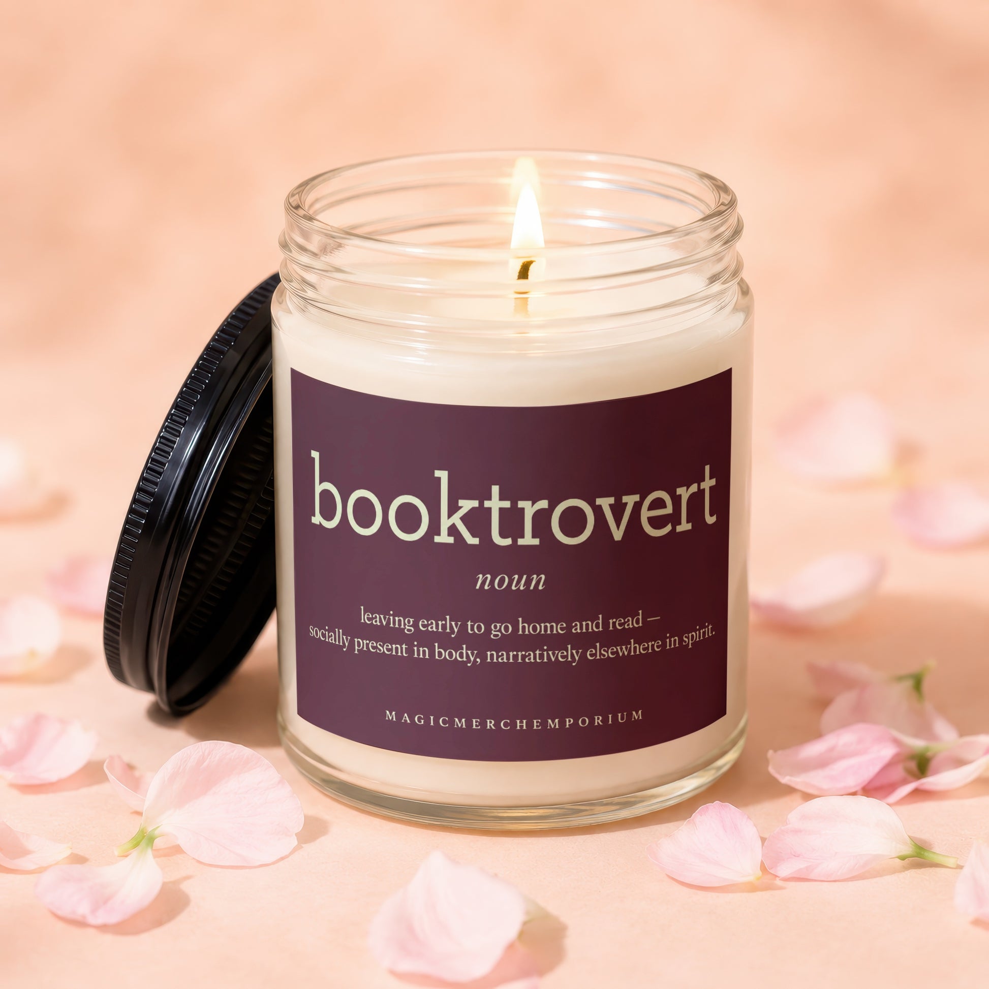 Lit candle with "booktrovert" definition on label, surrounded by pink petals.