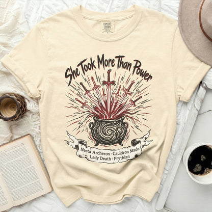Cream t-shirt with "She Took More Than Power" and a cauldron with swords graphic.