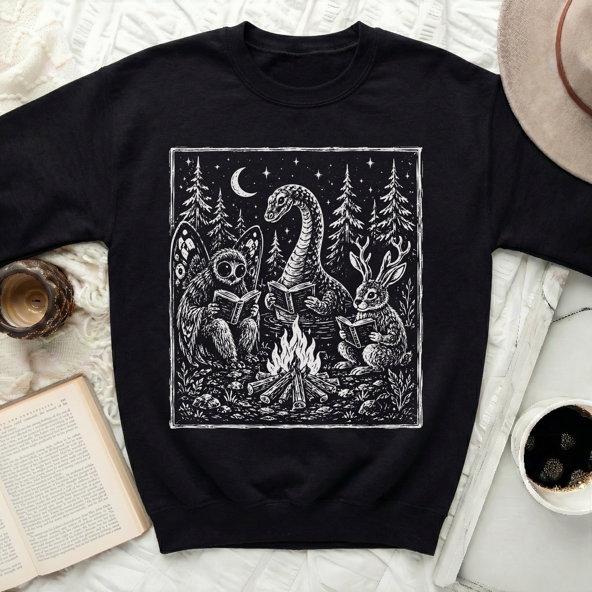 Black sweatshirt with white linocut print of mythical creatures reading around a campfire.