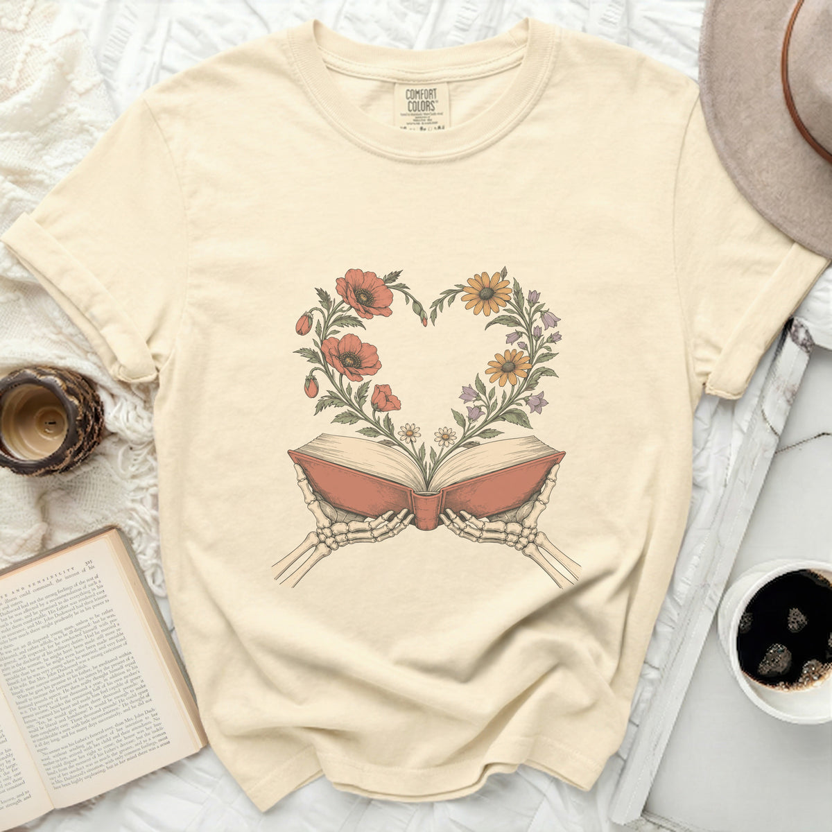 Skeleton hands hold an open book with a floral heart blooming from its pages.