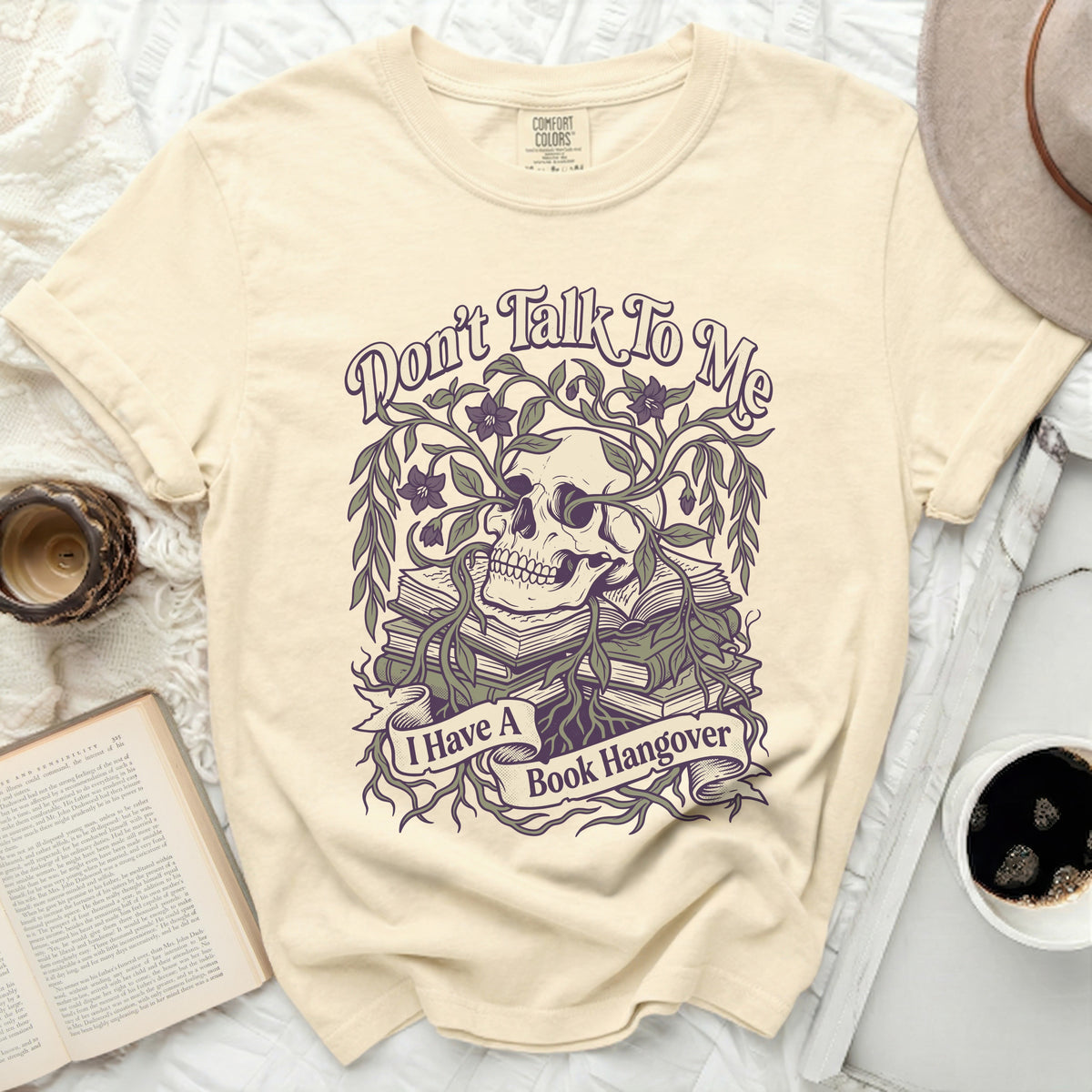 Cream t-shirt with a skull, books, flowers, and the text "Don't Talk To Me I Have A Book Hangover".