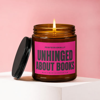 Amber candle with a lit wick and black lid, featuring a pink label that reads "Professionally Unhinged About Books".