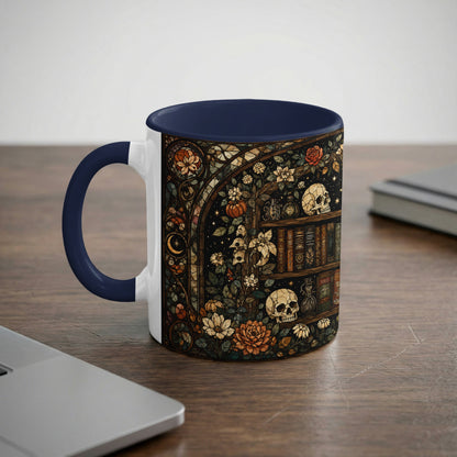 White mug with navy handle featuring gothic bookshelf, skulls, and floral stained glass design.
