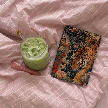 Phone case with tiger and floral design next to iced matcha drink on pink striped fabric.