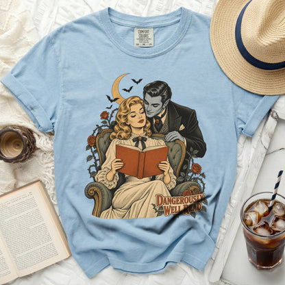 Light blue t-shirt with "DANGEROUSLY WELL READ" graphic of vampire and woman reading.