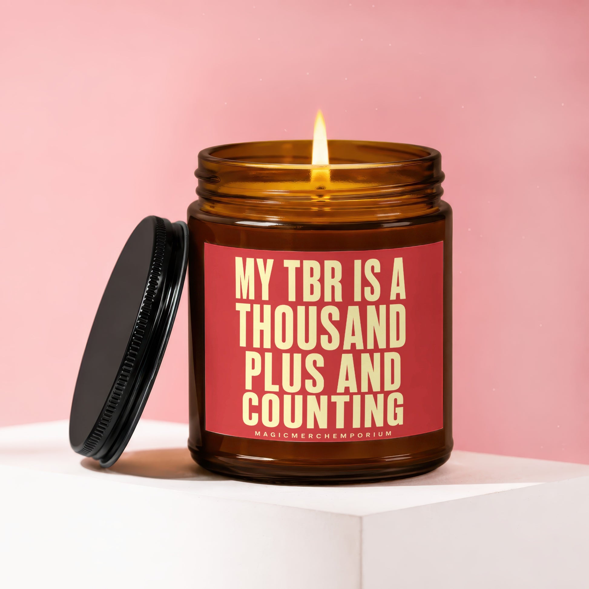 Amber candle with lit wick and red label reading "MY TBR IS A THOUSAND PLUS AND COUNTING".
