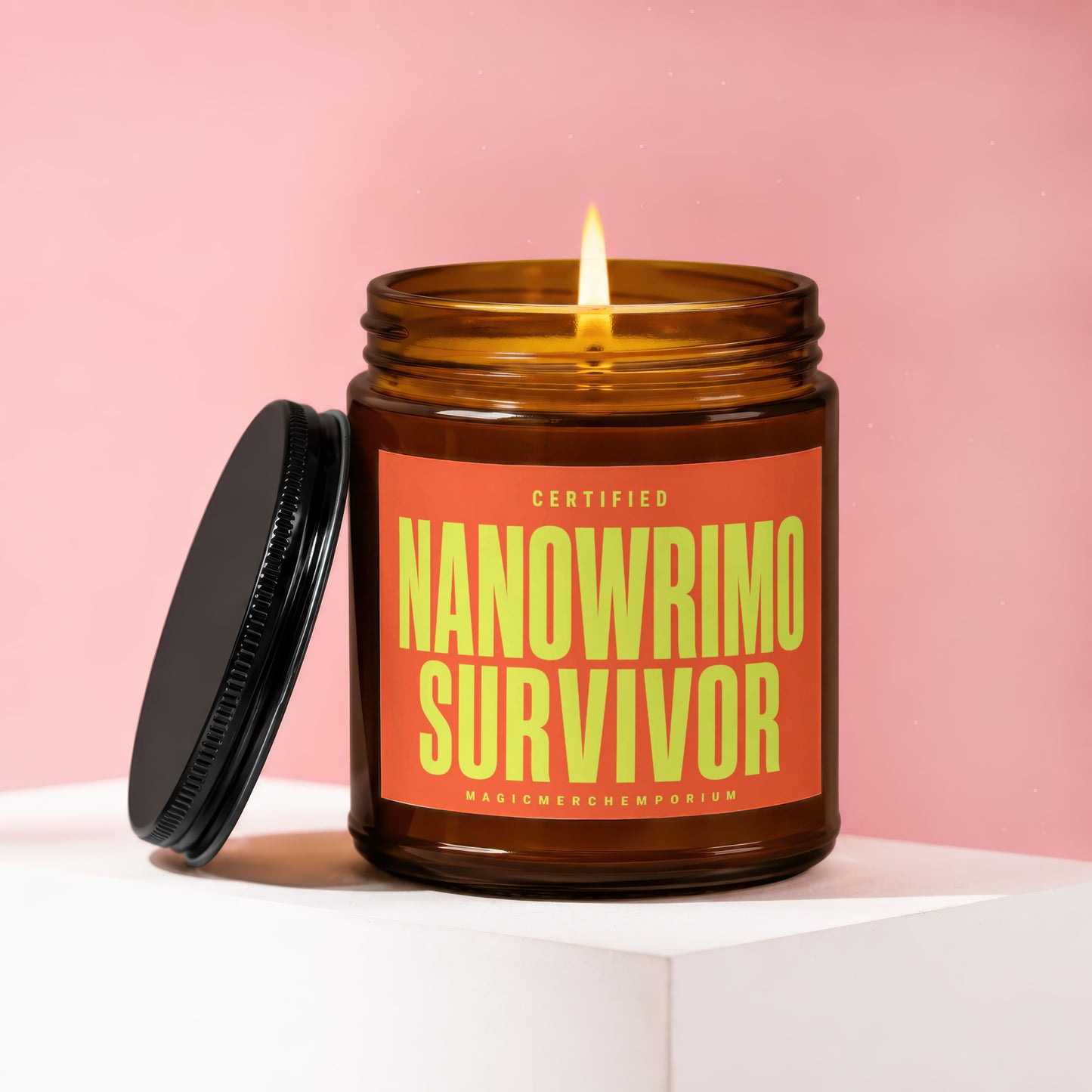 Amber glass candle with lit flame and lid beside. Text: "Certified Nanowrimo Survivor MagicMerchEmporium".