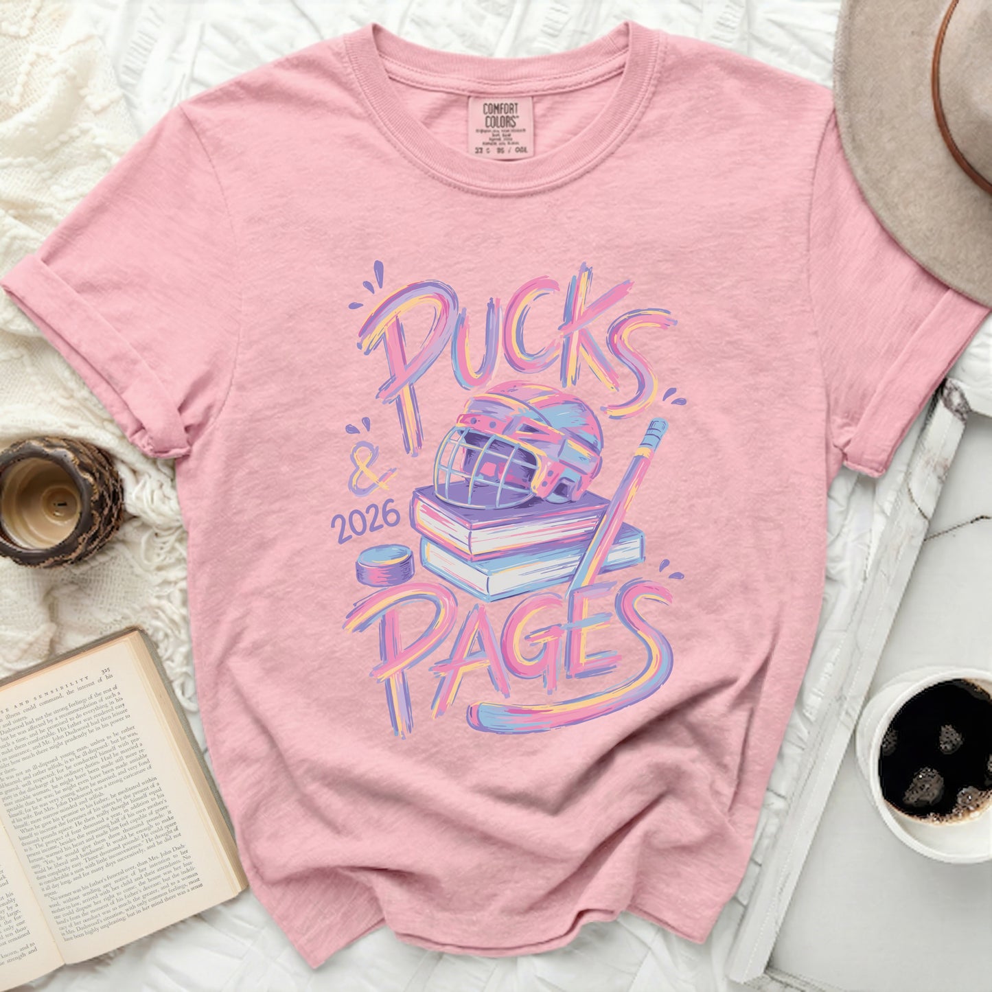 Pink t-shirt with "Pucks & Pages 2026" and hockey gear graphic.