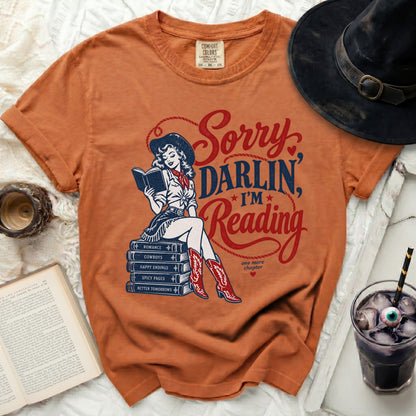 Orange t-shirt with a cowgirl reading a book on a stack of books.