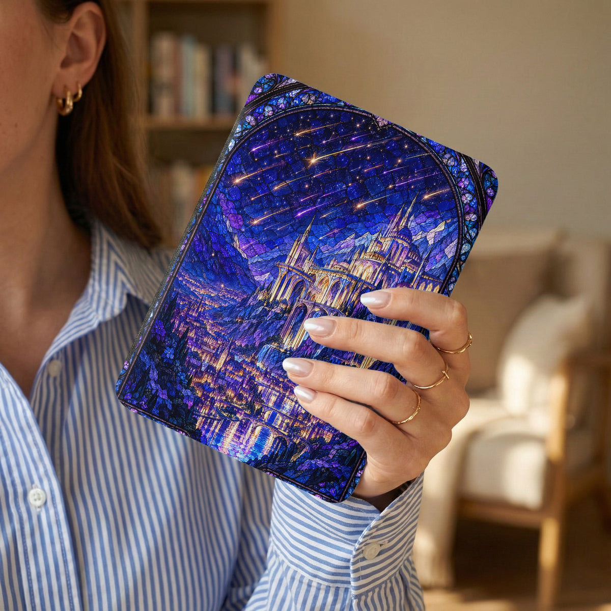 A person wearing a blue striped shirt holds a tablet case featuring a stained glass castle design under a starry blue night sky.