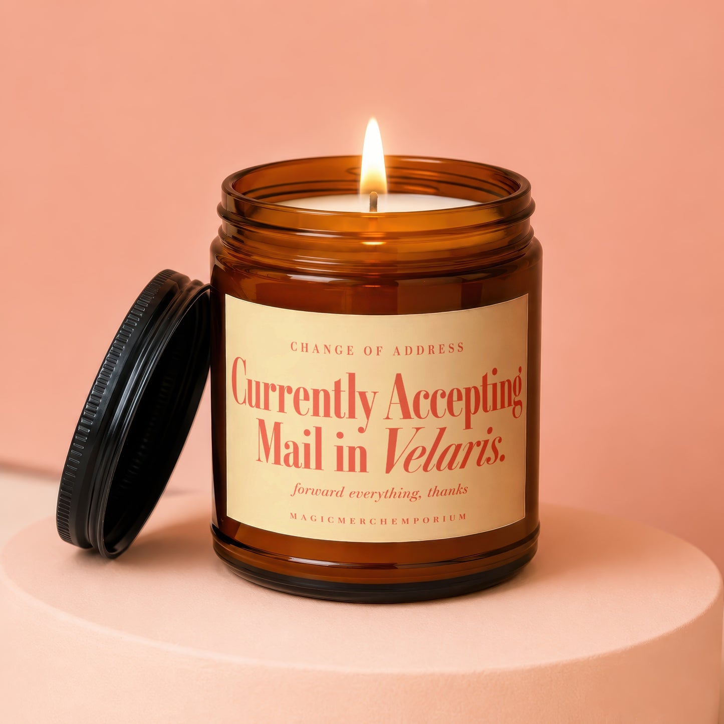A lit amber glass jar candle with a black lid resting beside it on a peach surface.