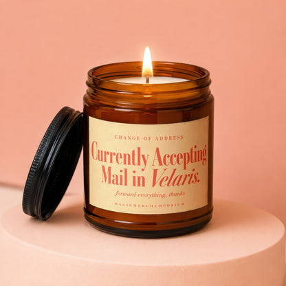 A lit amber glass jar candle with a black lid resting beside it on a peach surface.