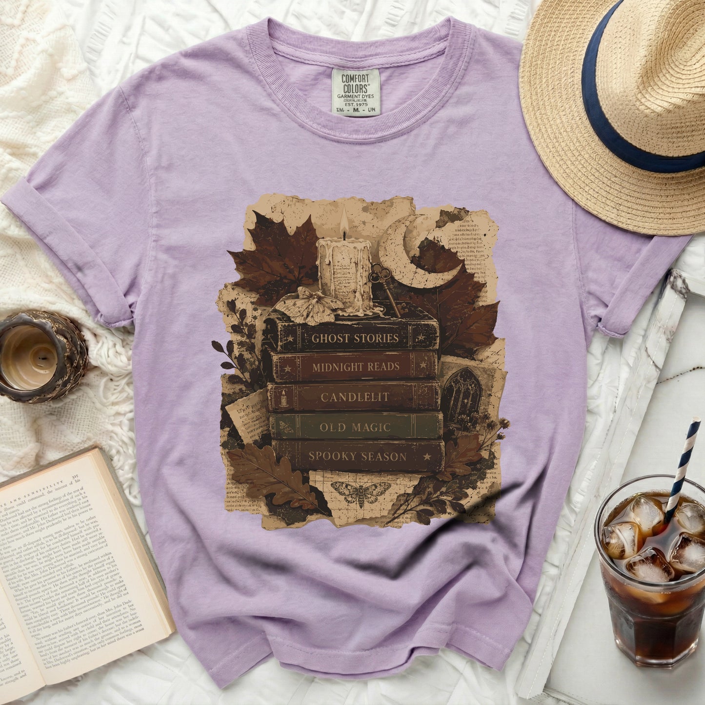 Lavender t-shirt with "Ghost Stories" graphic featuring books, candle, moon, and leaves.