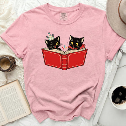 Pink t-shirt with illustration of two black cats reading a red book.