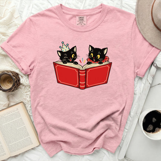 Pink t-shirt with illustration of two black cats reading a red book.