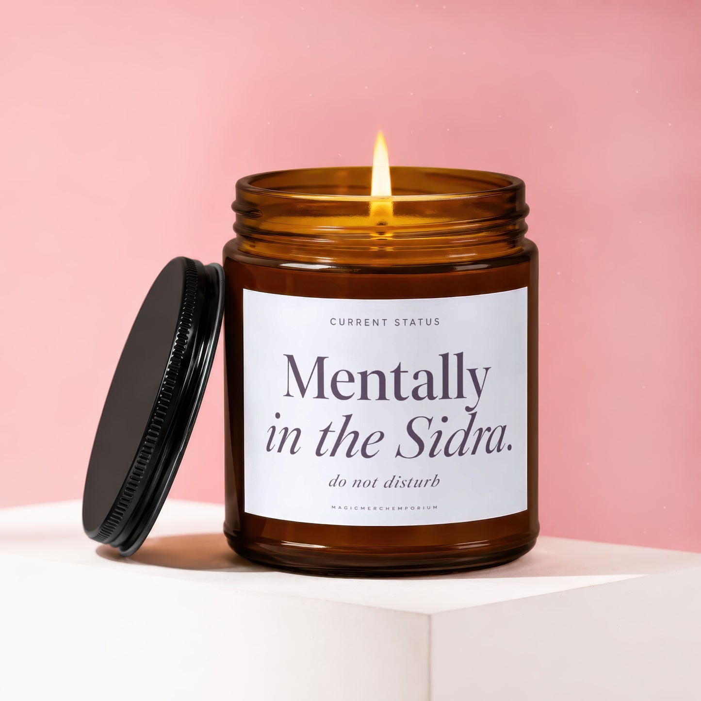 Amber glass candle with lit flame, label reads "Mentally in the Sidra. do not disturb."