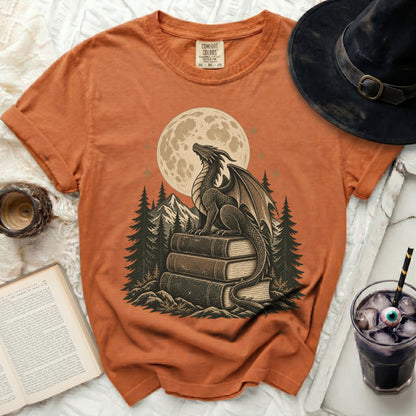 Orange t-shirt with a dragon sitting on books under a full moon.