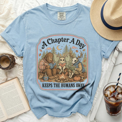 Bigfoot, moth, and deer skull reading by campfire text: A Chapter A Day Keeps Humans Away.
