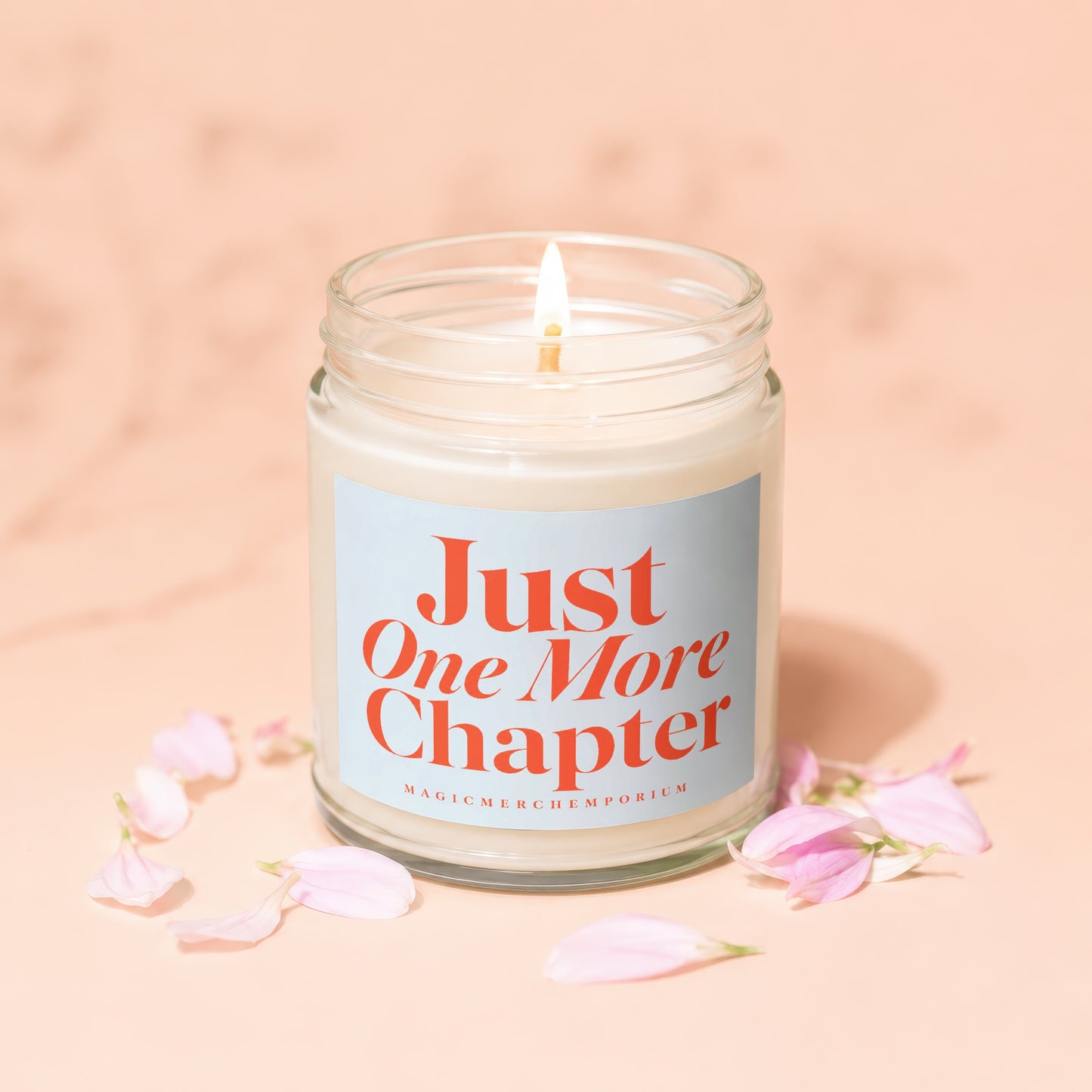 Lit candle in glass jar with "Just One More Chapter" text and pink petals.