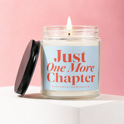 Glass candle with a lit wick, "Just One More Chapter" text on a blue label.