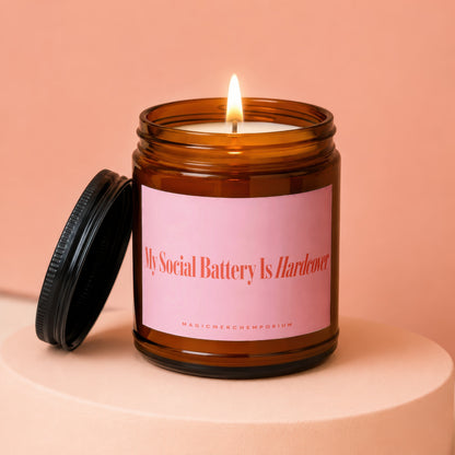 Candle in amber jar with pink label reading "My Social Battery Is Hardcover."