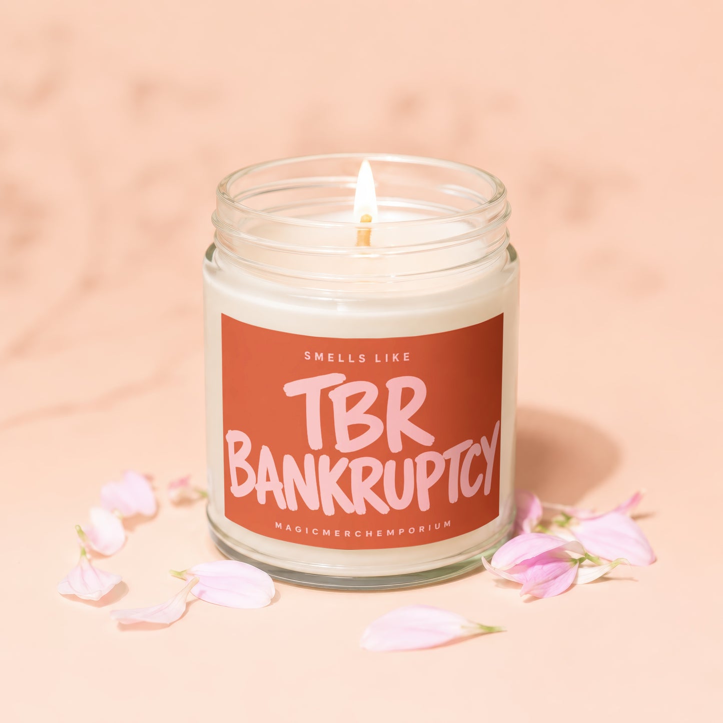 Candle that reads "Smells Like TBR Bankruptcy" with pink flower petals.