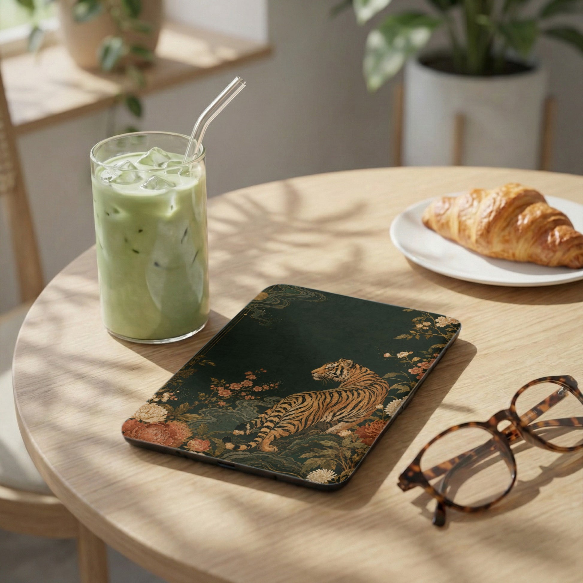 Tablet with tiger and floral print, next to iced matcha and croissant.