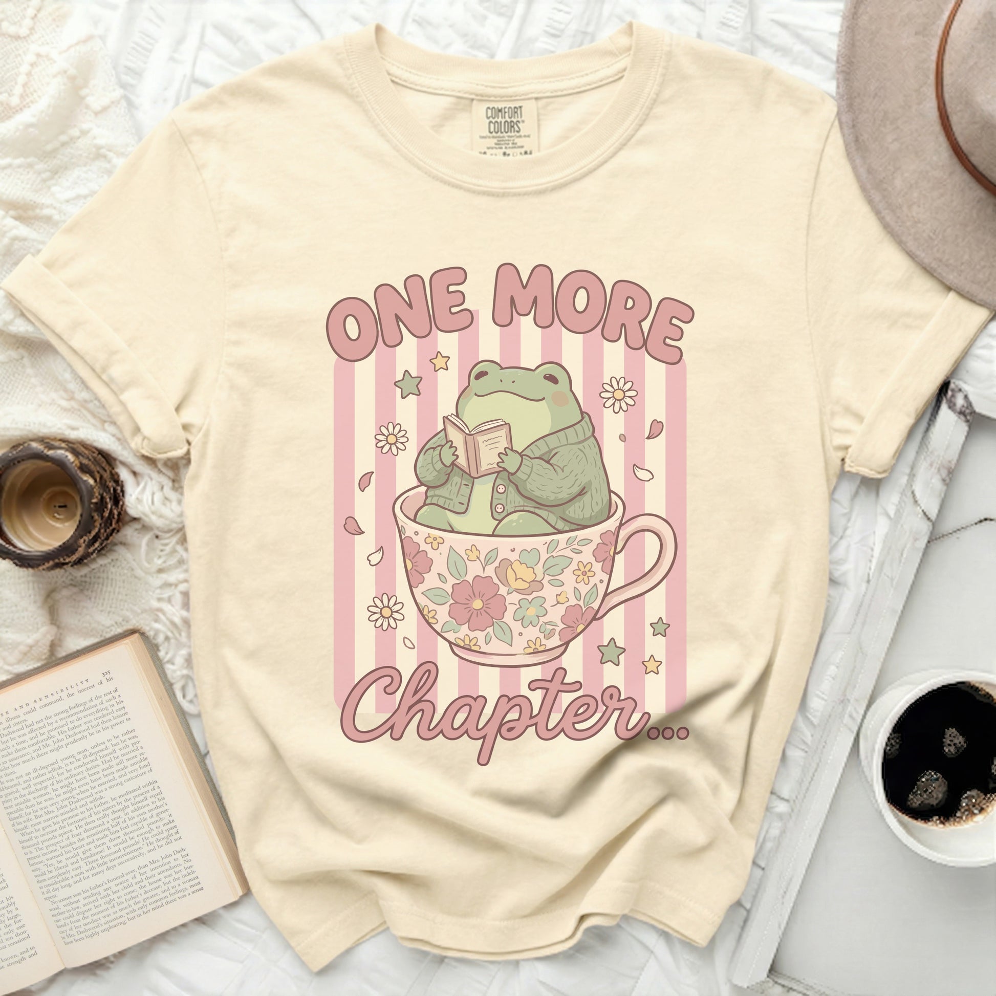 Cream t-shirt with frog reading in teacup graphic and "ONE MORE Chapter" text.