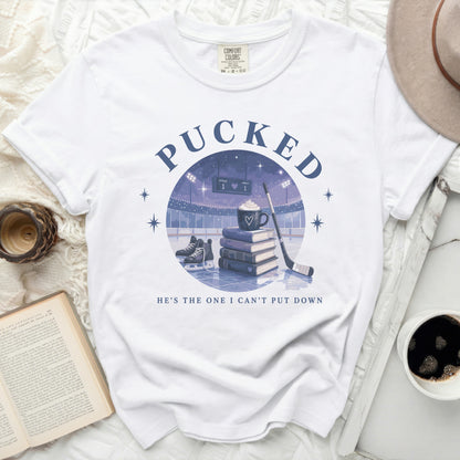 White t-shirt with "PUCKED" and hockey scene graphic, text "HE'S THE ONE I CAN'T PUT DOWN".