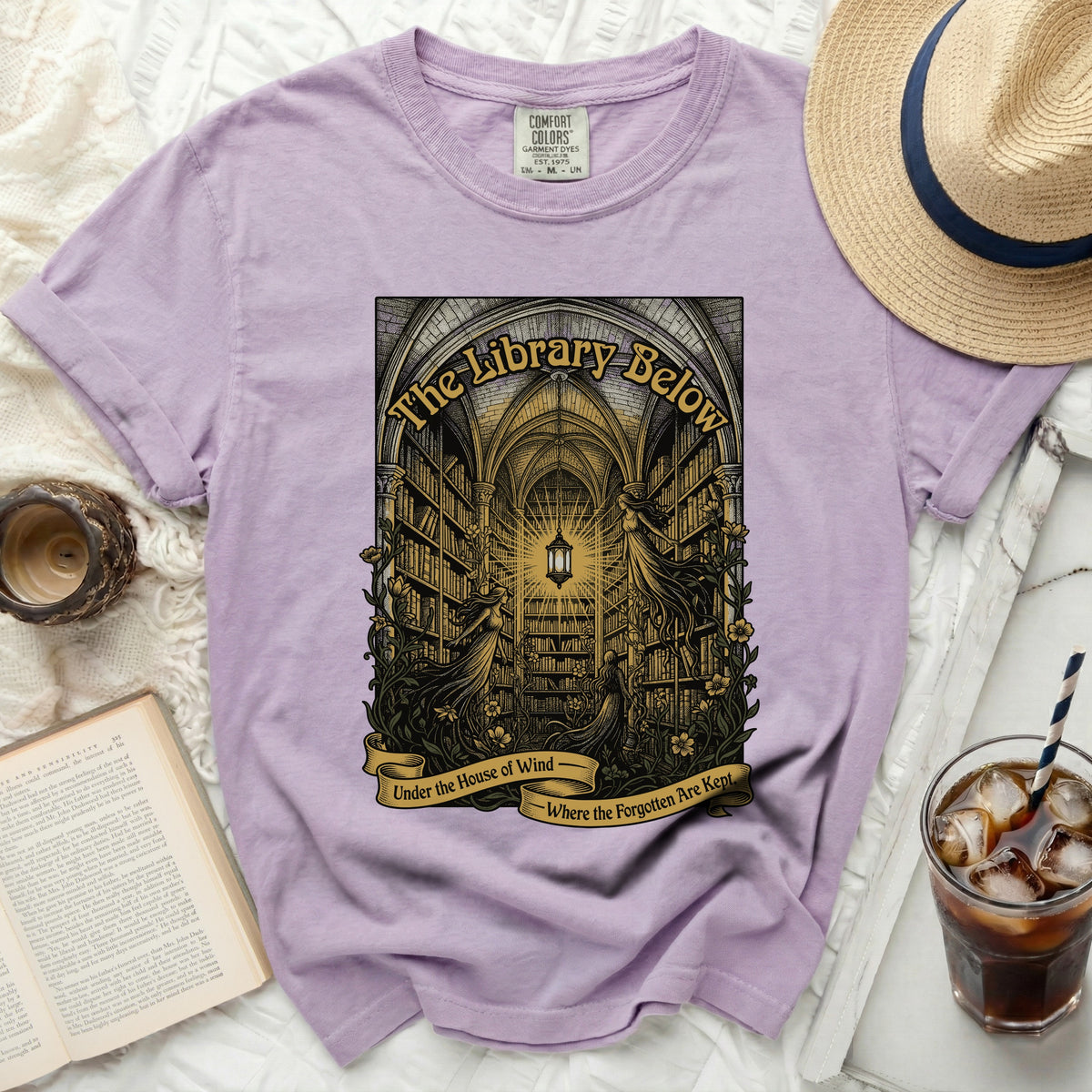 Lavender t-shirt with "The Library Below" print and text "Under the House of Wind Where the Forgotten Are Kept".