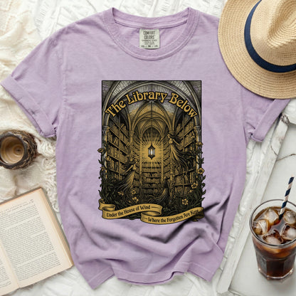 Lavender t-shirt with "The Library Below" print and text "Under the House of Wind Where the Forgotten Are Kept".