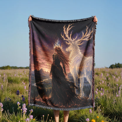 A person is holding a large blanket with a painting of a woman and a deer against a backdrop of a sunset and mountains.
